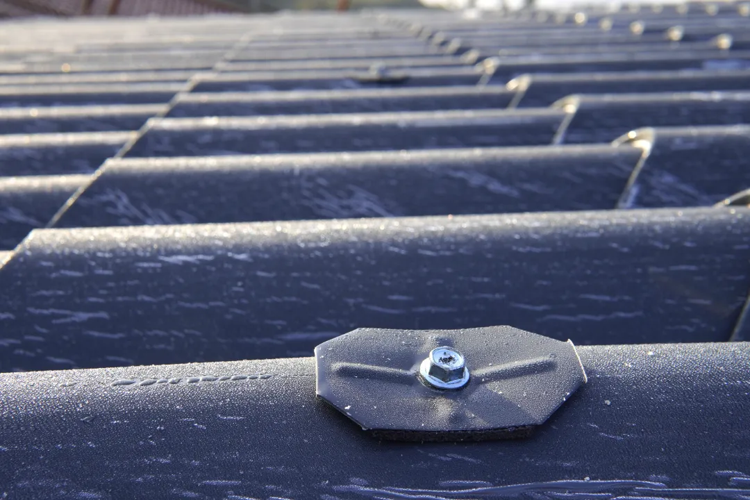 EPDM rubber roofing membrane close-up showing metal fixing clip and screw securing waterproof seam overlap